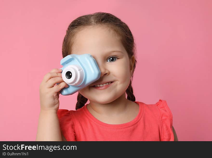 Little photographer taking picture with toy camera on pink background