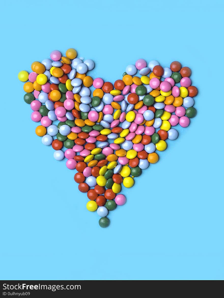 Colorful candies arranged as heart on blue background for valentines day, birthday, party card