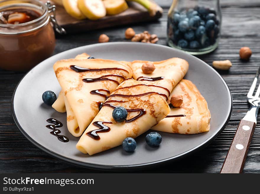 Delicious thin pancakes with chocolate, blueberries and nuts on black wooden table