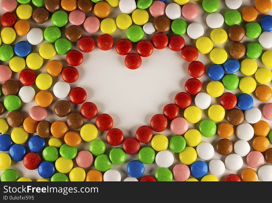 Colorful dragee beans in the shape of a heart on a white background. Decoration background. Closeup.