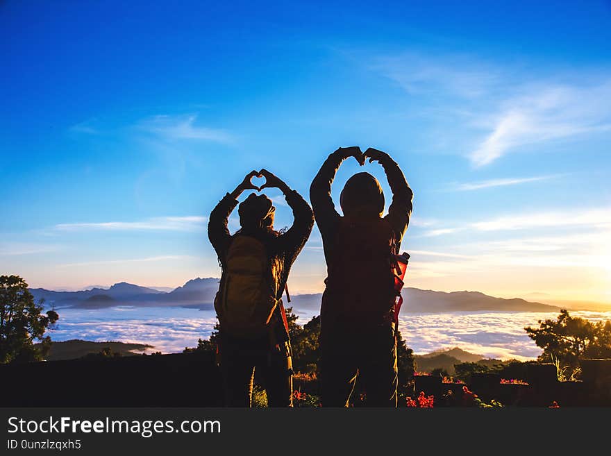 Lover women and men asians travel relax in the holiday. Stand up for sunrise on the Moutain,happy honeymoon,Raised his hand to make a heart shape.