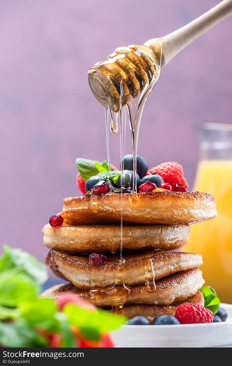 Pouring Honey on Pancakes Stack Topped with fresh Fruits. Shrove Tuesday Breakfast.