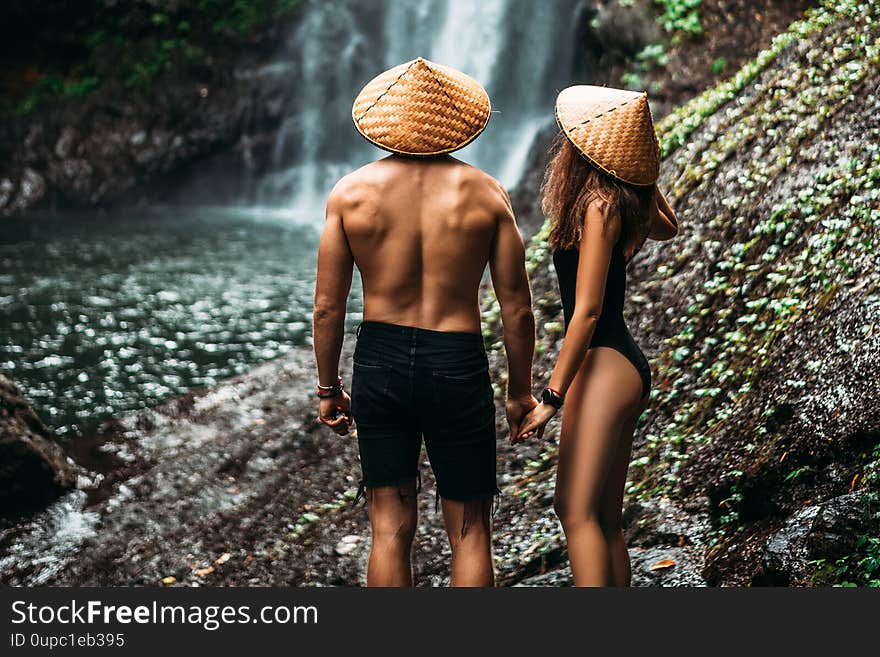 Lovers at the waterfall, rear view. Couple admiring a beautiful waterfall in Indonesia. Couple on vacation in Bali. Honeymoon trip