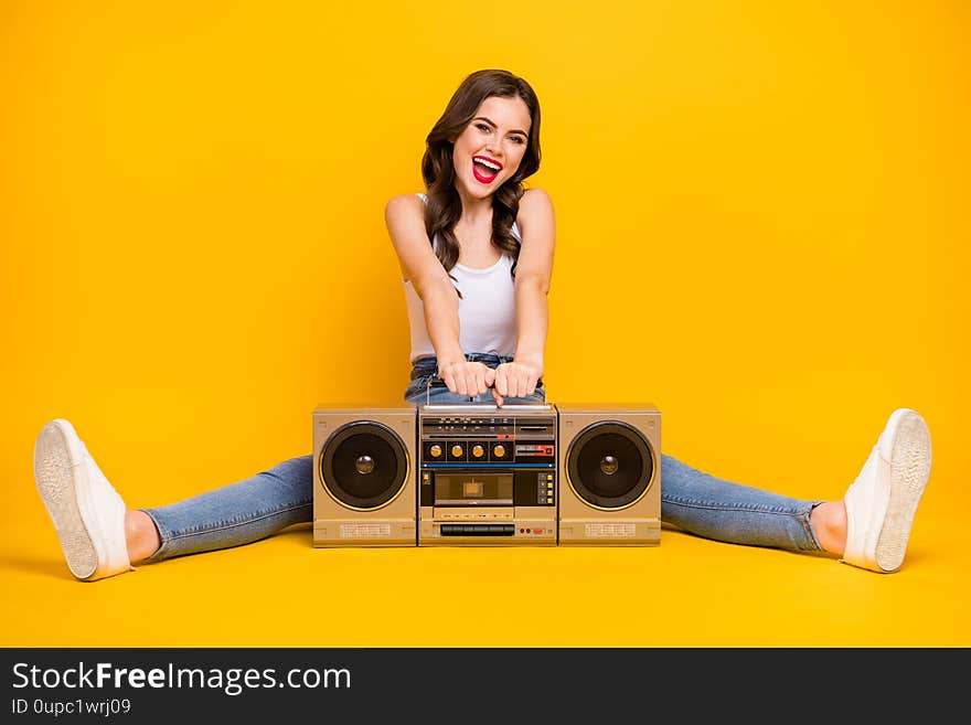 Full length photo of pretty crazy lady sit floor vintage recorder between spread legs party mood wear white tank-top jeans shoes, isolated bright yellow color background