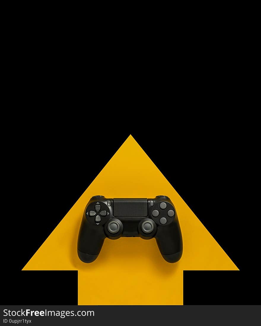 Modern black gamepad on a yellow arrow on a black background. Joystick on a yellow direction indicator on a dark background. Flat lay copyspace