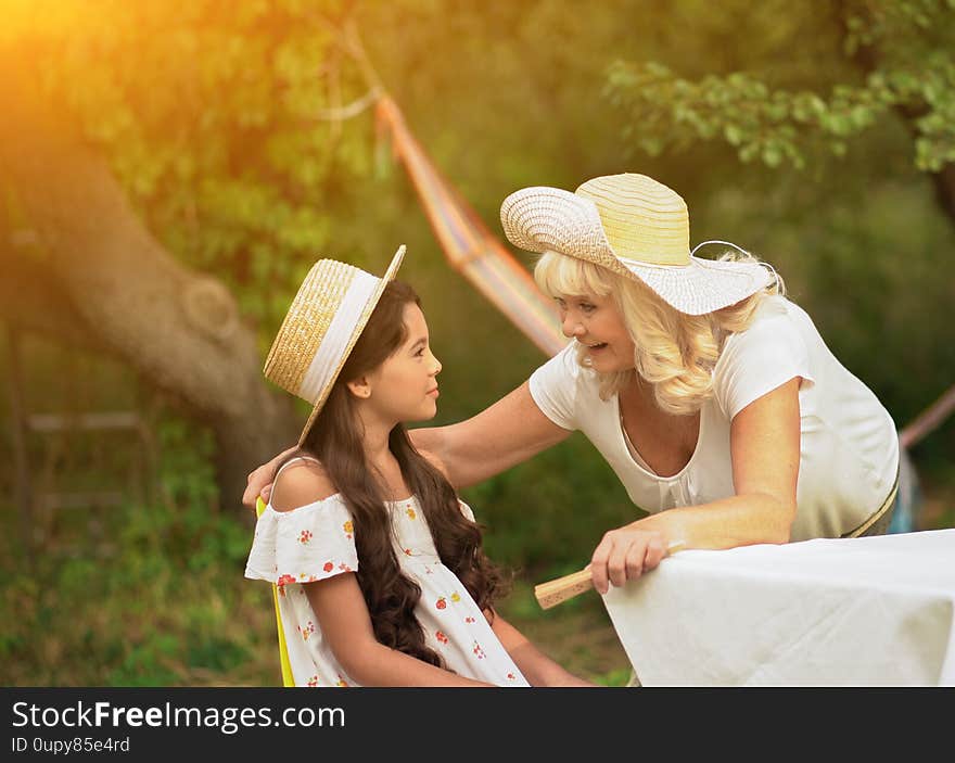 Grandmother speak to little girl sitting on chair in garden. Old lady has conversation with granddaughter outdoor across park. Grandmother speak to little girl sitting on chair in garden. Old lady has conversation with granddaughter outdoor across park.