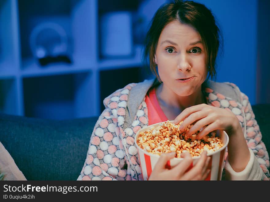 Young lady is watching TV laughing and eating popcorn having fun at home alone enjoying modern television. Youth lifestyle and cheerful people concept.