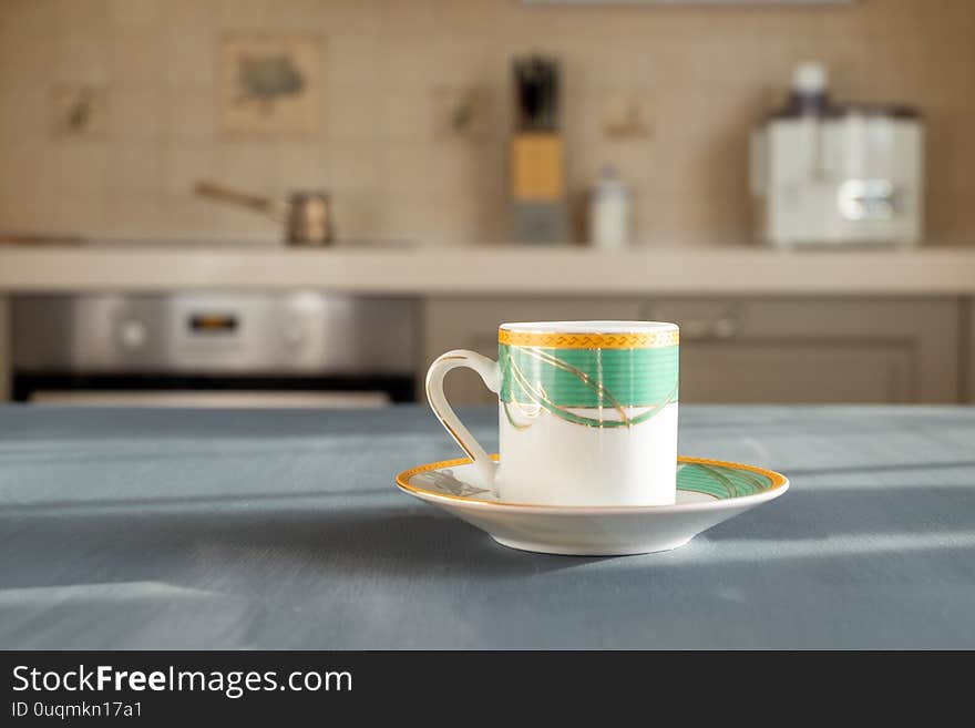 Fine porcelain coffee or teacup on a wooden surface of dark gray graphite color on a blurry background of the interior of a cozy kitchen on a sunny morning or afternoon. Horizontal orientation. Fine porcelain coffee or teacup on a wooden surface of dark gray graphite color on a blurry background of the interior of a cozy kitchen on a sunny morning or afternoon. Horizontal orientation