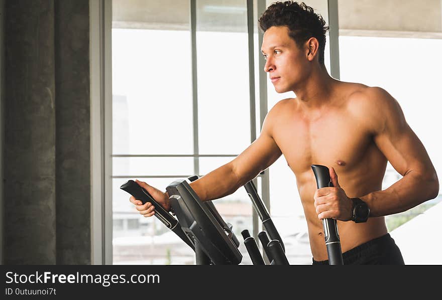 Young man at the gym exercising on the cross trainer machine. Fitness man doing cardio workout program