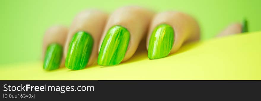 Female fingers with lime manicure holding green paper on yellow background