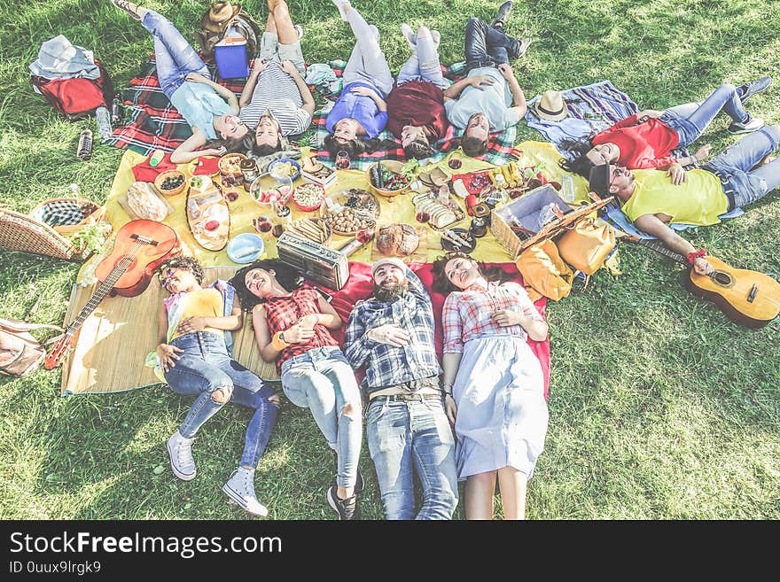 Happy friends lying down at picnic with barbecue on city park outdoor - Young people eating enjoying time together in summer time - Focus on bottom guys