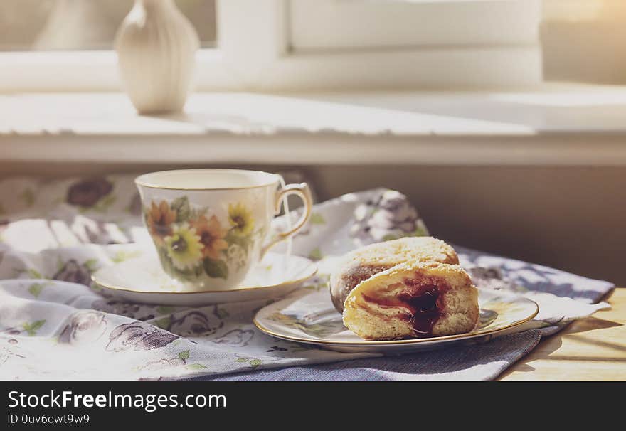 Selective focus of home made jam doughnuts with burry background of cup of hot blueberry tea, Soft focus of afternoon tea served with strawberry jam donut in sunny day summer, English traditional