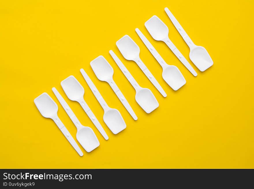 White plastic spoons on yellow background. Fast food, eco and no plastic concept. Top view. Copy, empty space for text.