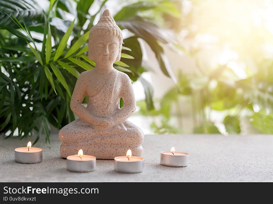 Natural stone statue of Buddha sitting in meditation surrounded by candles and tropical plants