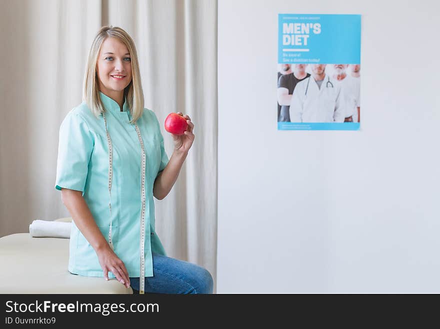 Beautiful dietitian is standing in the office holding an apple