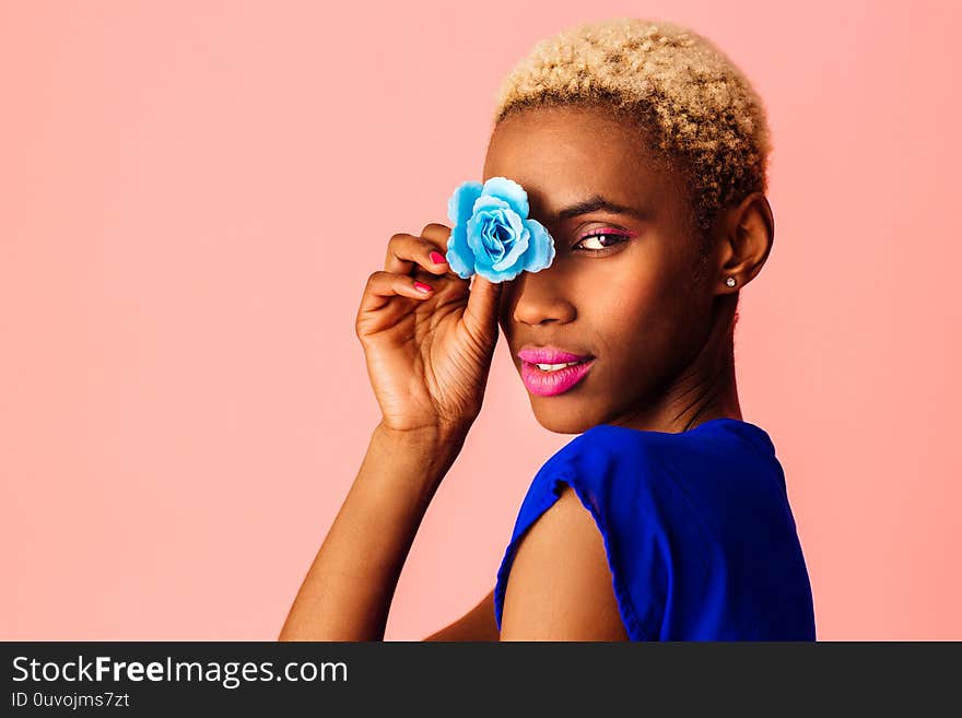 Beautiful young woman covering eye with blue rose flower