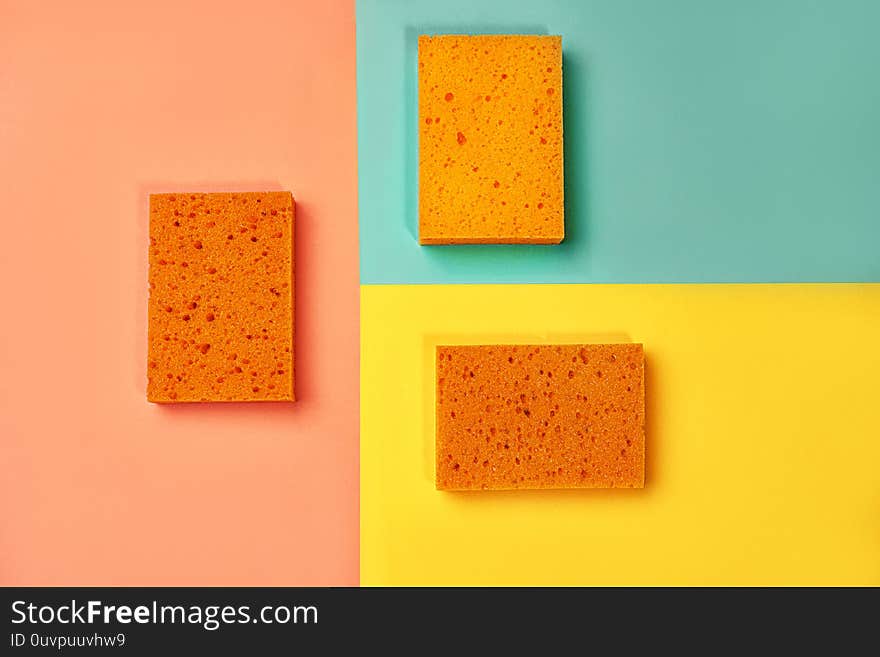 Trendy collage made of orange color sponges on yellow, pink coral and trendy mint green blue background. Flat lay, top view, close up. Minimal style.