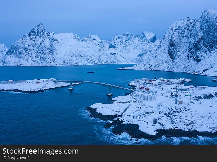 Aerial view of Norwegian fishing village in Reine City, Lofoten islands, Nordland, Norway, Europe. White snowy mountain hills, nature landscape background in winter season. Famous tourist attraction