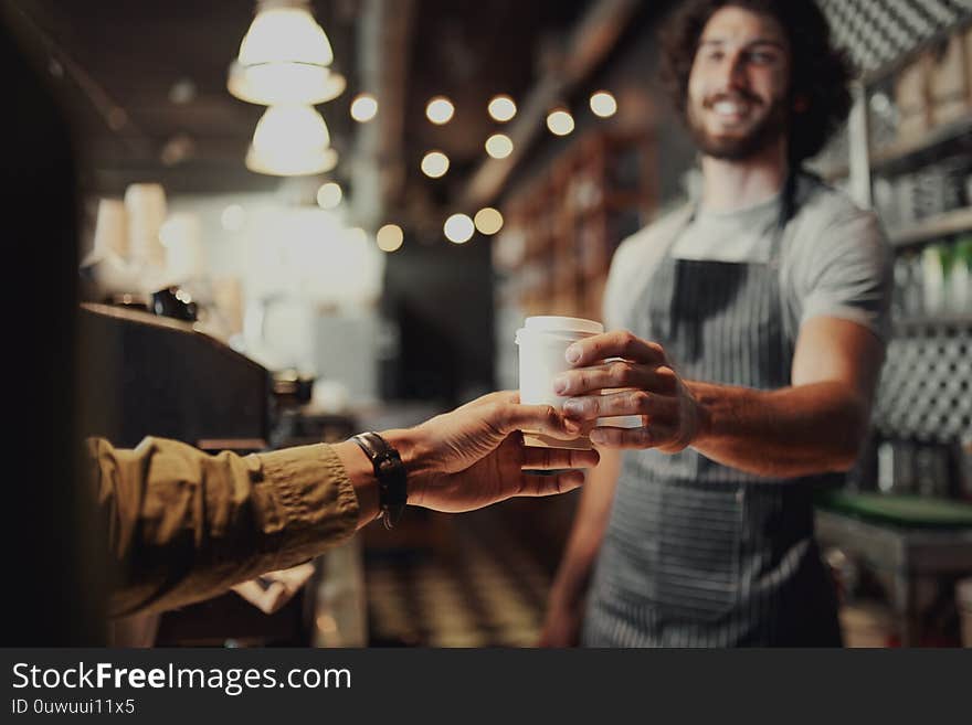 Young men waiter standing in cafe gives the coffee to men client. Young men waiter standing in cafe gives the coffee to men client