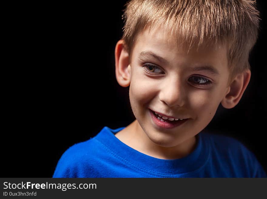 Portrait the face of the boy `s smiling child close-up against a black background. Emotions. Portrait the face of the boy `s smiling child close-up against a black background. Emotions