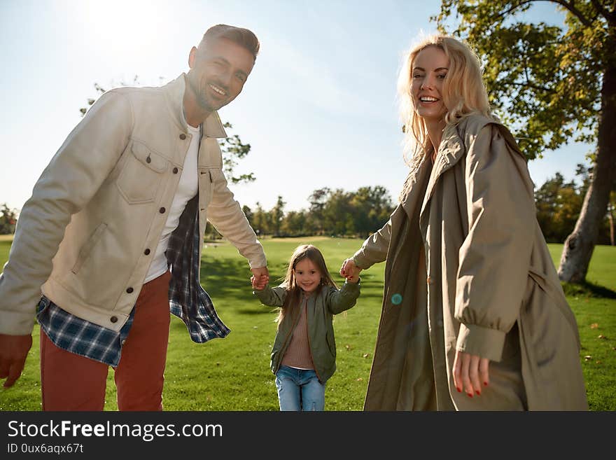 Portrait of cheerful parents playing with their child in a green park as they enjoy the tranquility of nature. Family, parenthood, and leisure concept. Horizontal shot. Front view. Portrait of cheerful parents playing with their child in a green park as they enjoy the tranquility of nature. Family, parenthood, and leisure concept. Horizontal shot. Front view