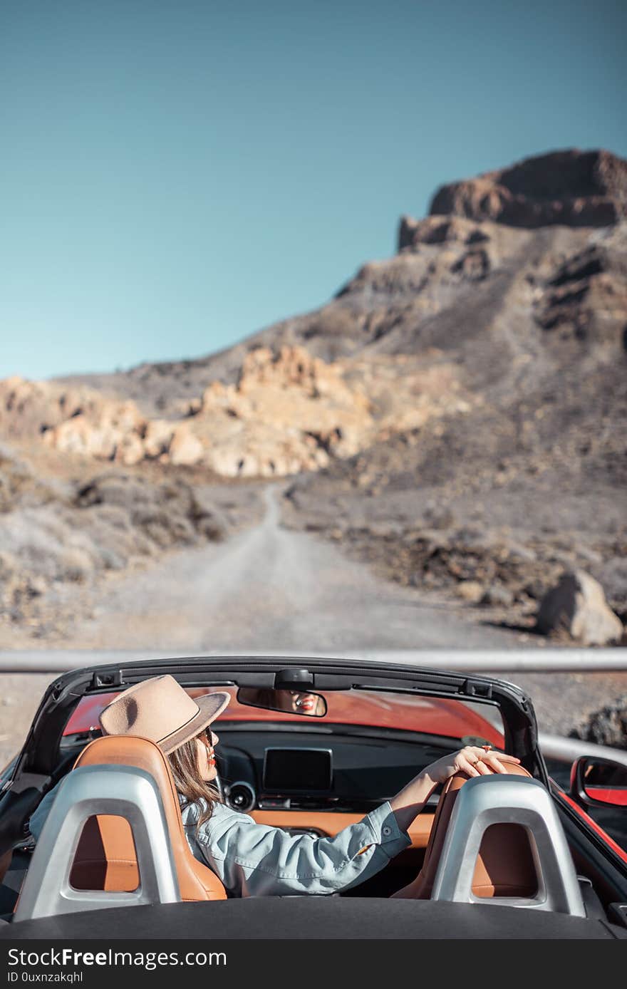 Young woman traveling by convertible car on the picturesquare road on the desert valley, rear view. Carefree lifestyle and travel concept. Young woman traveling by convertible car on the picturesquare road on the desert valley, rear view. Carefree lifestyle and travel concept