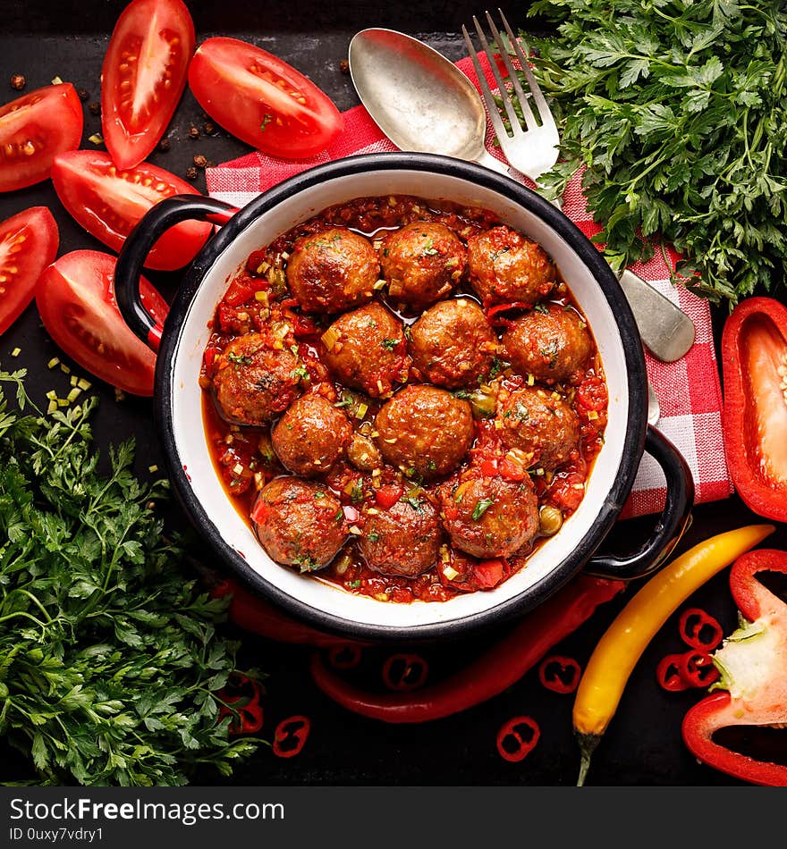Meatballs in tomato sauce with the addition of aromatic herbs in an enamel dish, top view