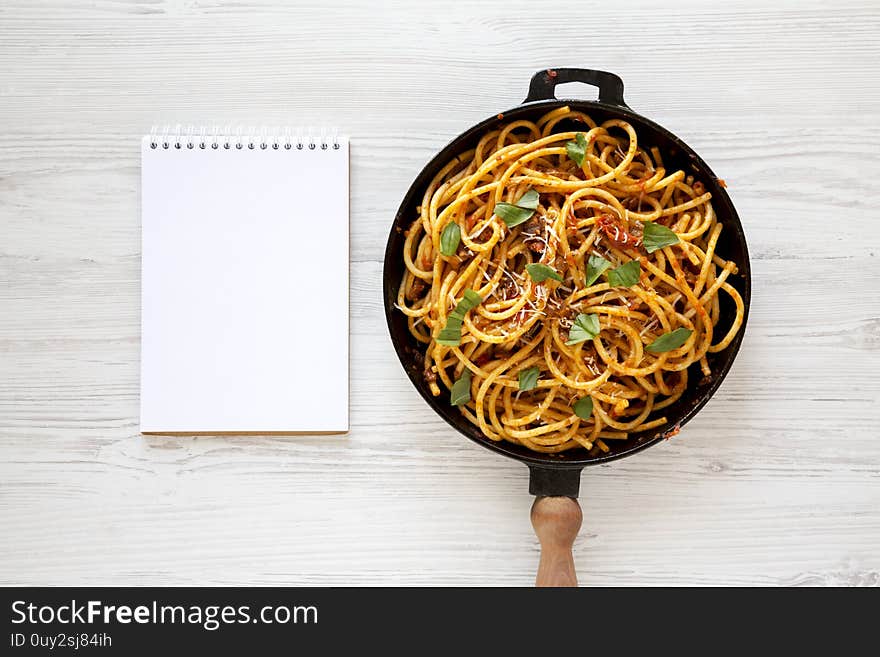 Homemade Bucatini all Amatriciana Pasta in a cast iron pan, blank notepad on a white wooden background, top view. Flat lay, overhead.