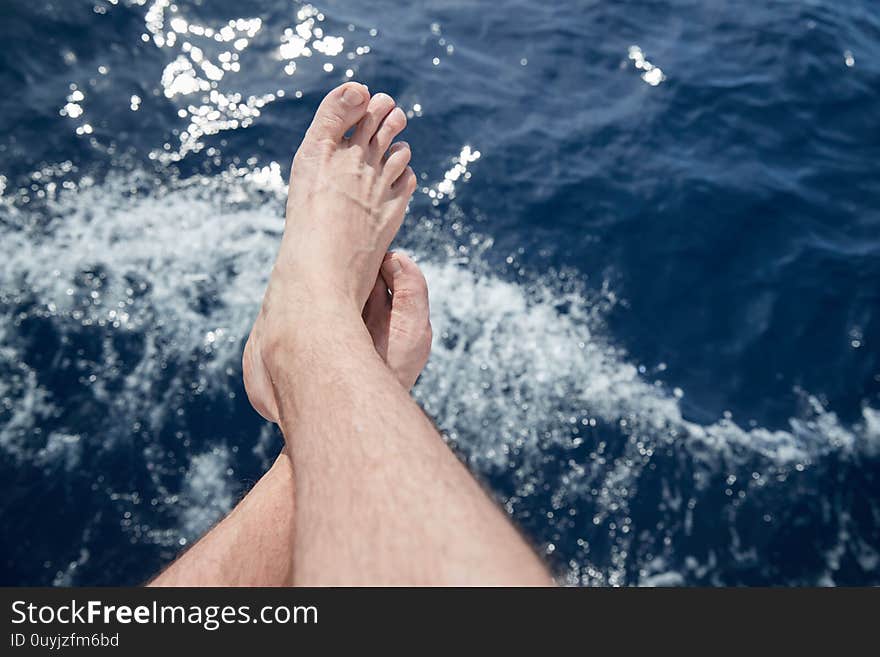 Bare feet hang down over azure water, splashes, sun patches of light on water,  sailing, sunny weather, sun reflections, summer