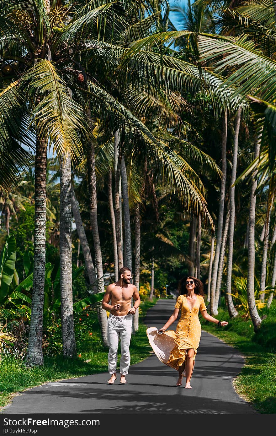 Beautiful couple running among palm trees in Bali, Indonesia. Honeymoon on the Islands. A happy couple in love runs along the road