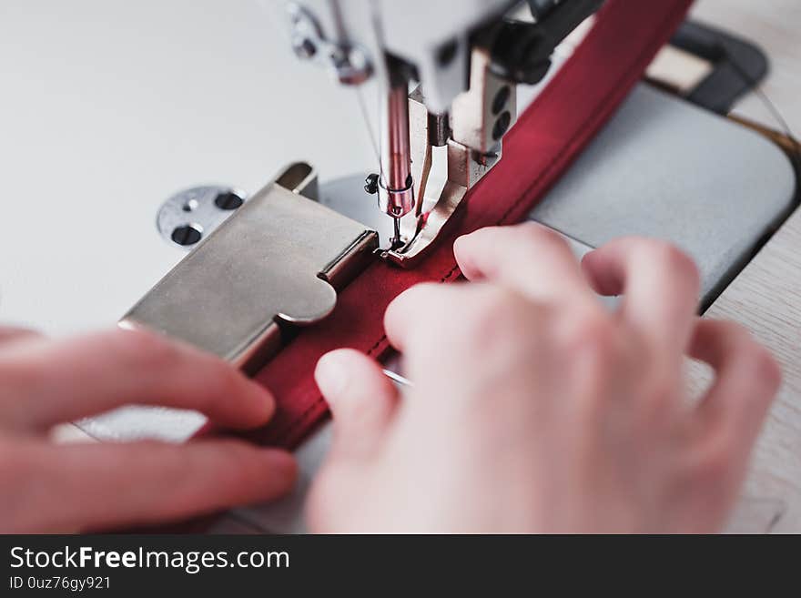 A leather craftsman produces leather goods on a sewing machine in his shop. Handmade work. Close up