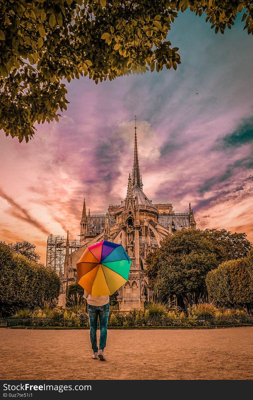 Young woman walking at Notre Dame Paris France ,sunset colors Notre Dame Paris, rainbow umbrella during sunset