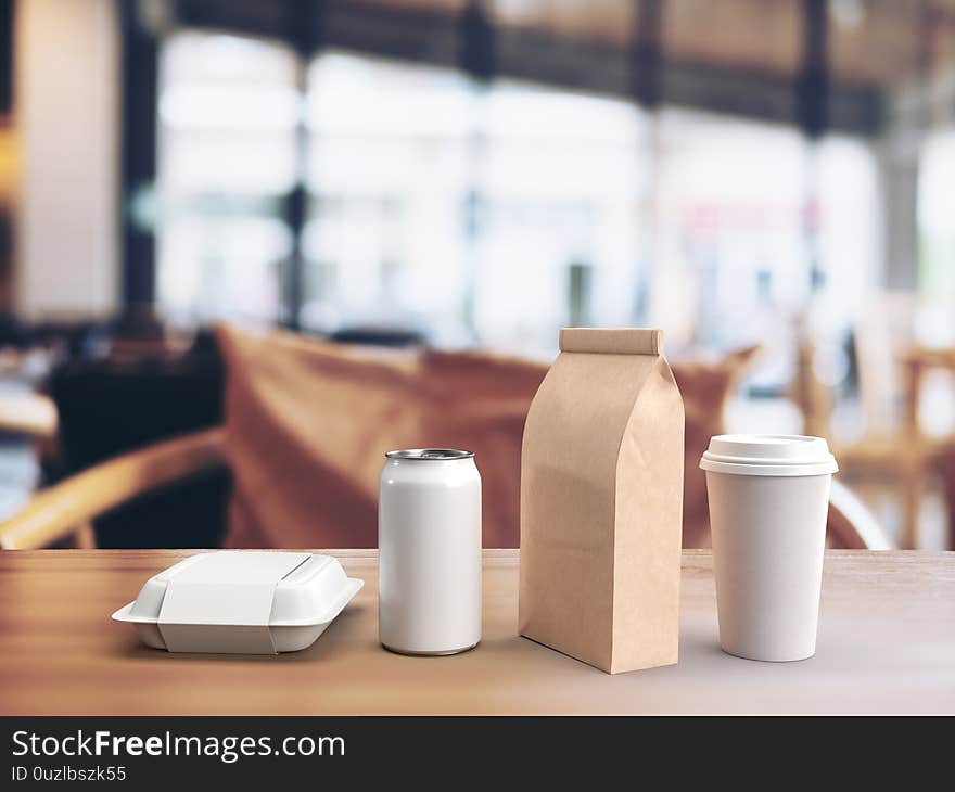 3d render of white mockup of a takeout lunch box, beverage can, paper coffee bag and coffee mug on a wooden table in a blurred restaurant background.