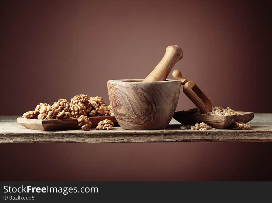 Walnuts in a wooden dish on an old wooden table. Crushed and whole nuts near the mortar. Brown background, copy space. Walnuts in a wooden dish on an old wooden table. Crushed and whole nuts near the mortar. Brown background, copy space