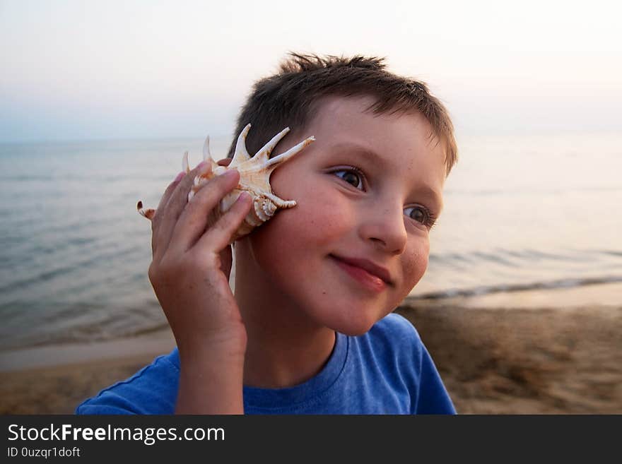 Pensive boy listens to a seashell on the seashore. Good hearing concept.