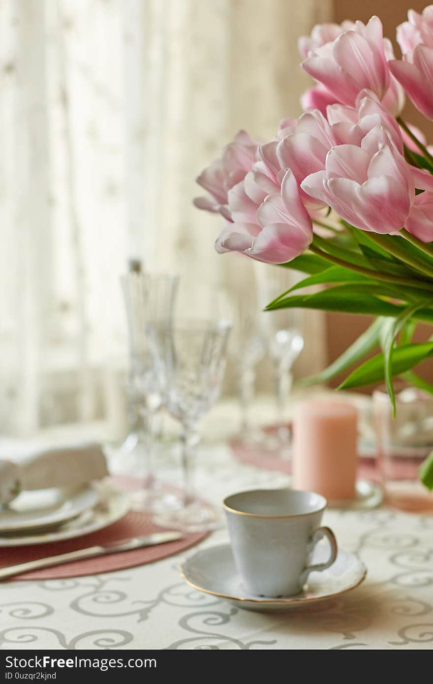 Decor and spring table setting is a vase with pink tulips and dishes of white color. Selective focus.