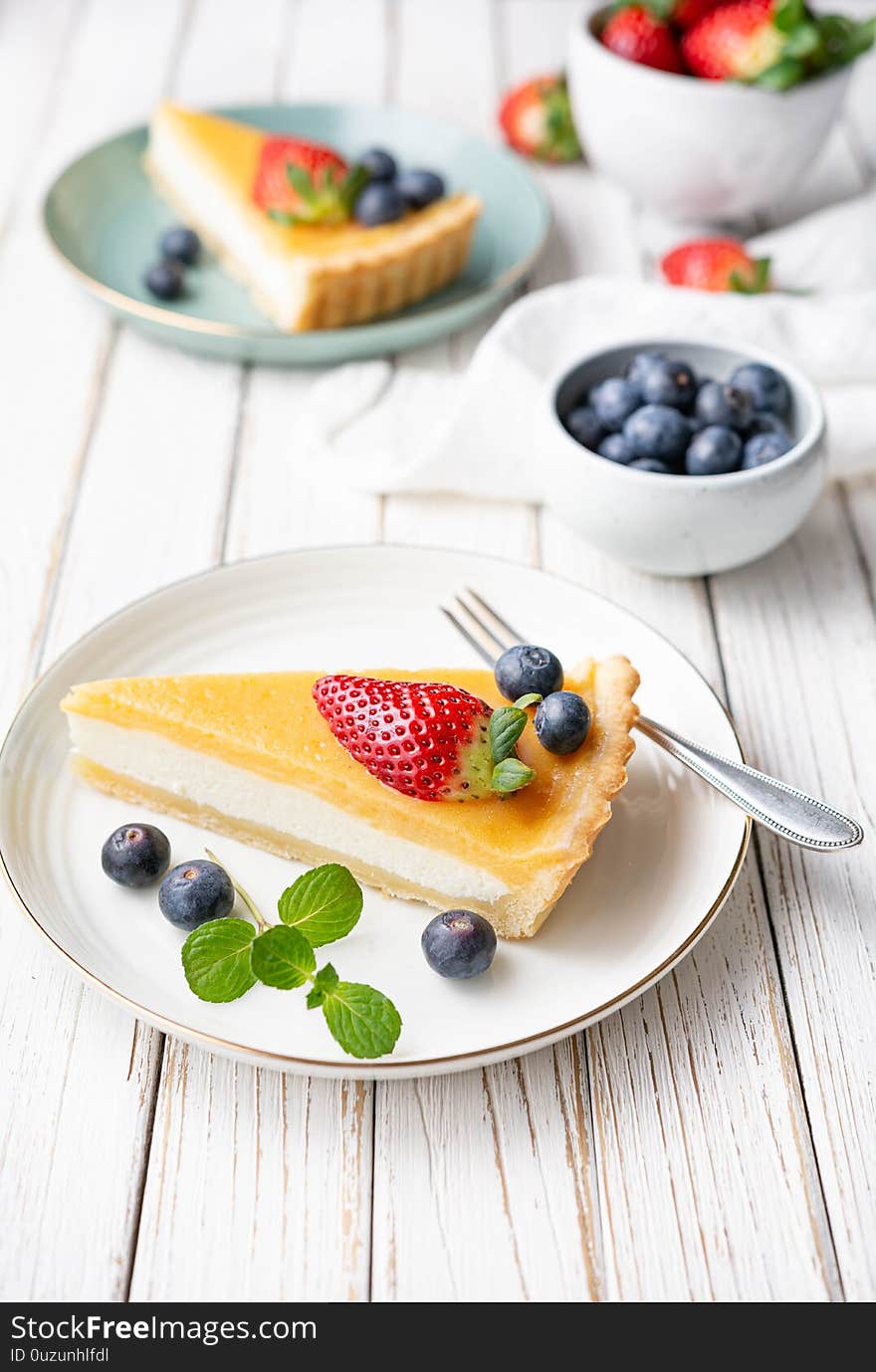 Cream cheese tart slices with lemon curd topping, served with fresh blueberries and strawberries on white rustic background