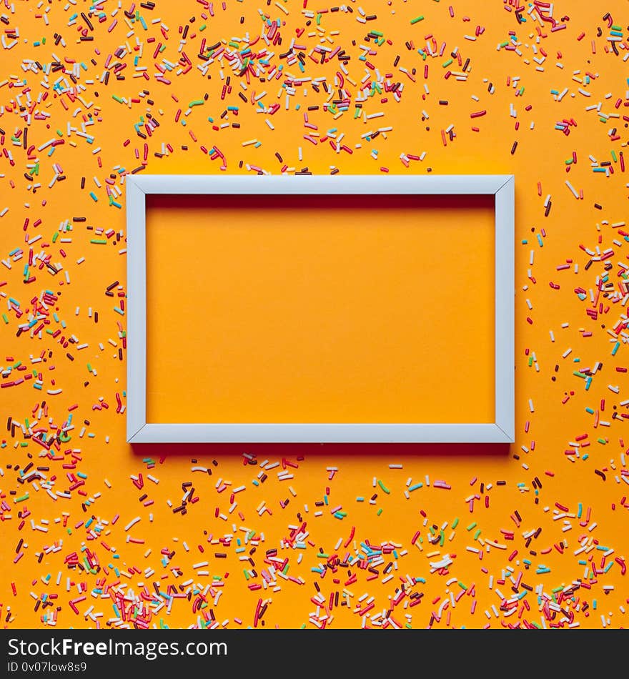 White frame and colorful sprinkles for cakes on orange background. Birthday party concept. Mock up, place for text