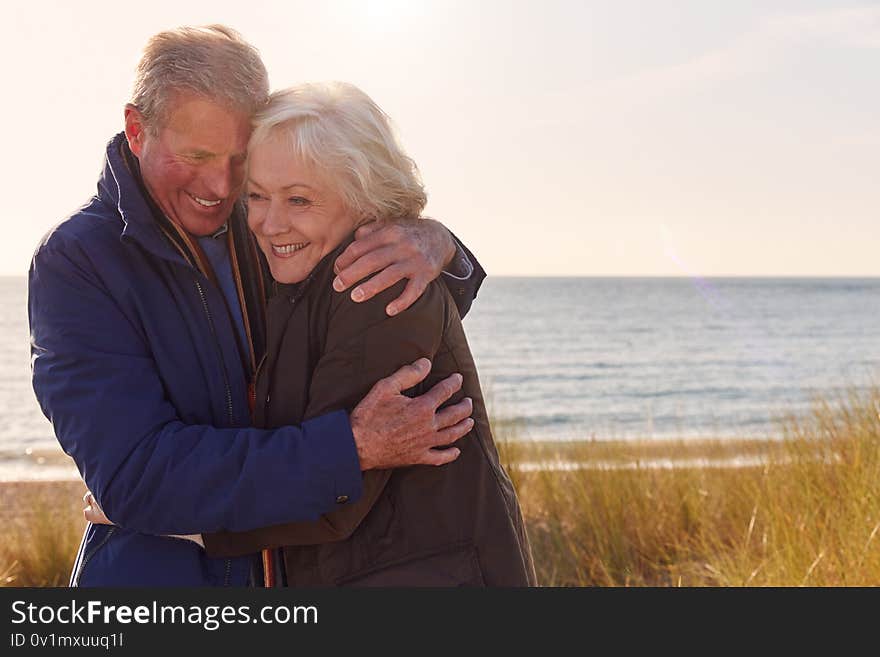 Loving Active Senior Couple Hugging As They Walk Through Sand Dunes