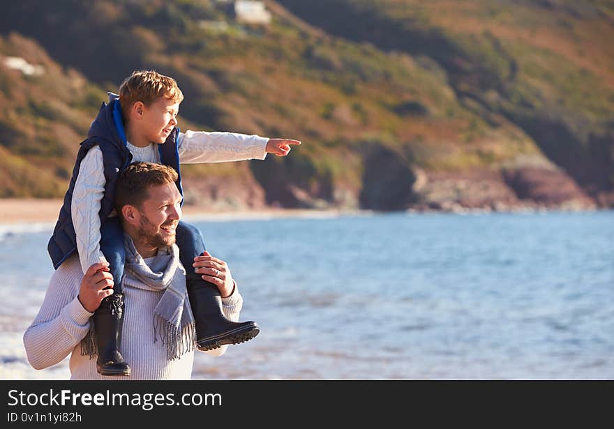 Father Giving Son Ride On Shoulders As They Walk Along Beach By Sea