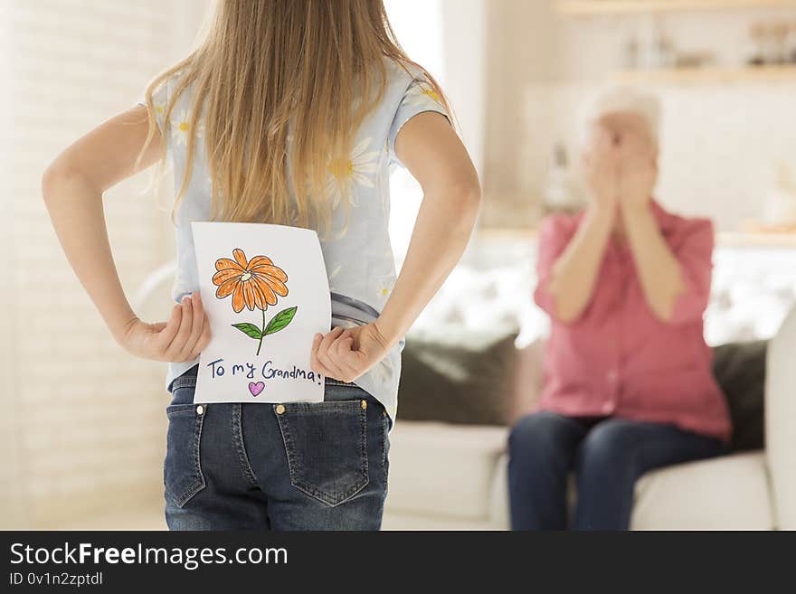 Family celebration. Little girl with greeting card for granny behind her back, closeup. Empty space