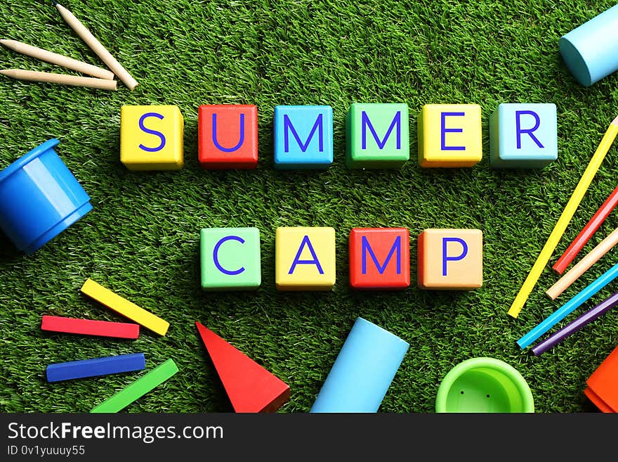 Flat lay composition with phrase SUMMER CAMP made of colorful cubes on green grass