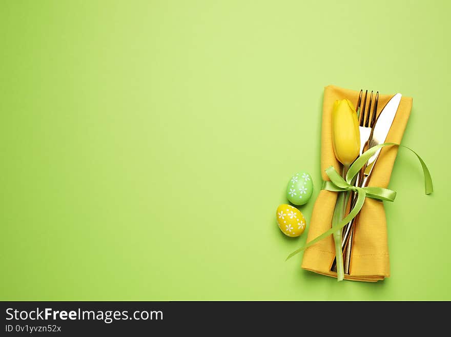 Top view of cutlery set with floral decor on green background, space for text. Easter celebration