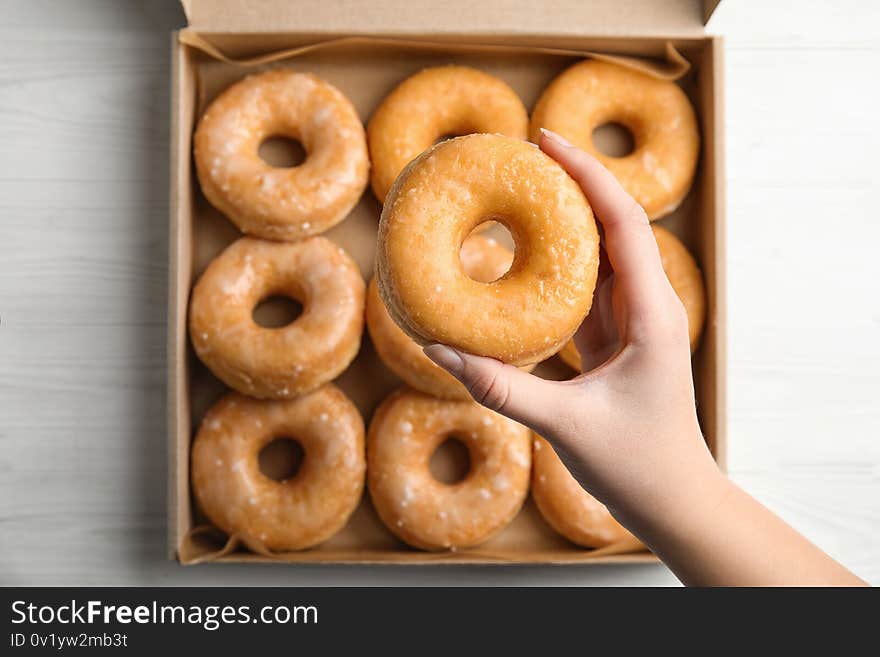 Woman holding delicious donut at white wooden table, top view