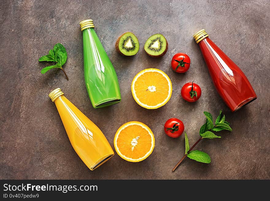 Flat lay a variety of bottled juices and halves of fruits and vegetables on a dark rustic background. Assorted juices, tomato, orange, kiwi. View from above.