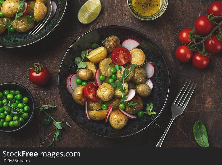 Baby potatoes salad with green peas and radish, black background, top view