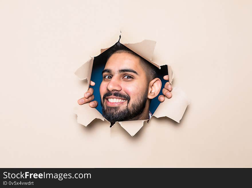 Young handsome indian bearded man smile look from beige paper hole