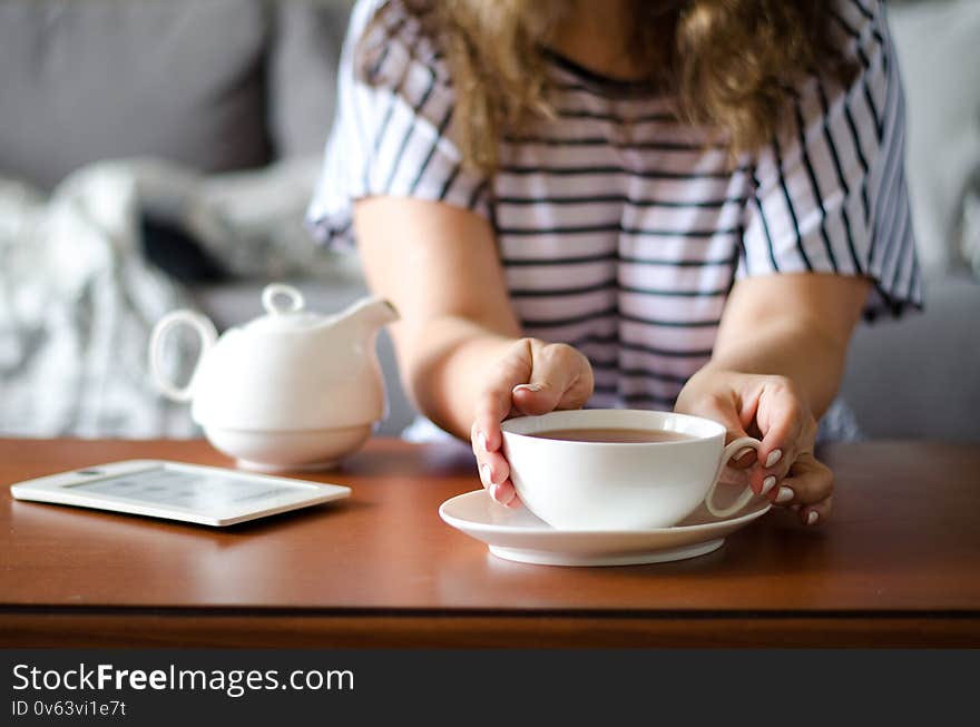 Cozy home interior with teapot, eBook and woman holding cup of tea. Horizontal. Cozy home interior with teapot, eBook and woman holding cup of tea. Horizontal