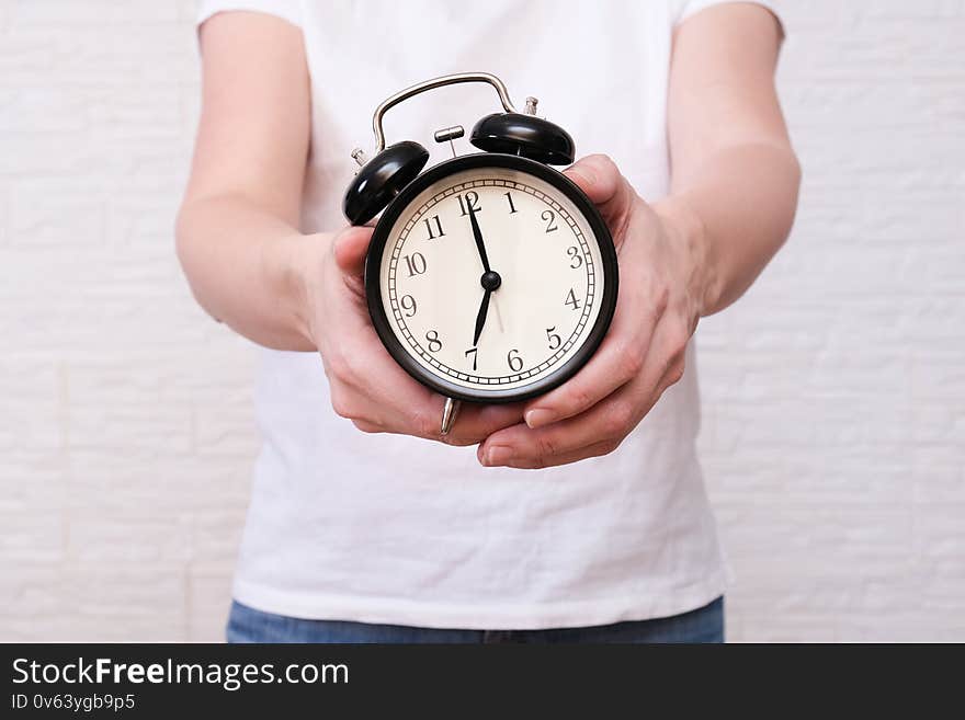 Woman holding an alarm clock in hands, the time is 7 am, early morning waking up