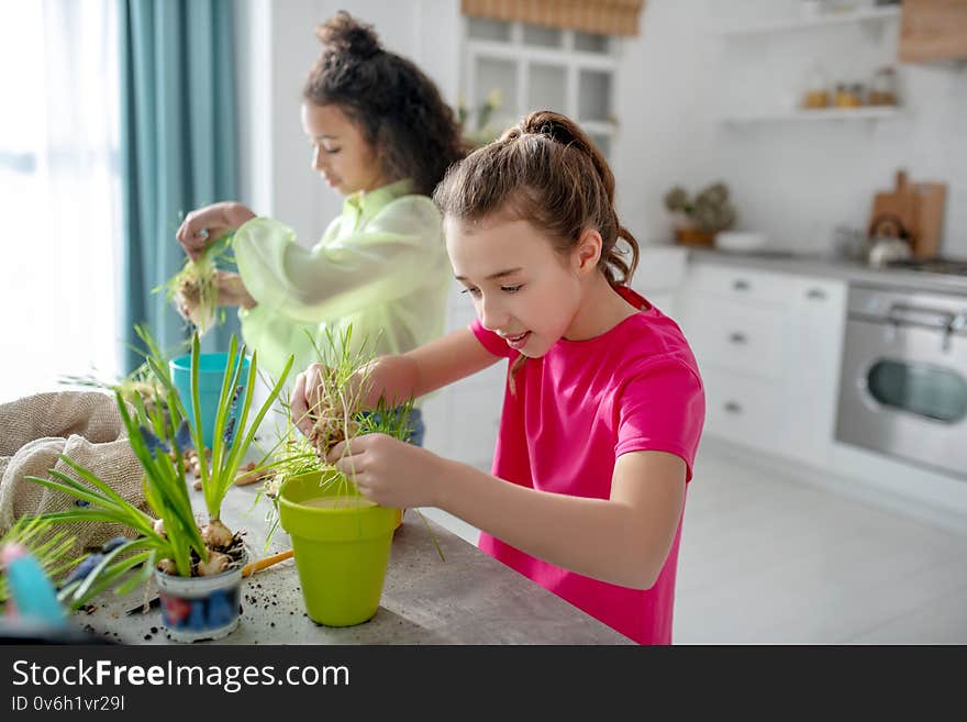 Two girls standing near the table with plants in their hands.